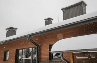 A close-up of a snow-covered roof and gutter with chimneys during winter snowfall, highlighting winter architecture.